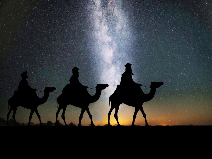 three silhouettes of men on camels against a starry night sky