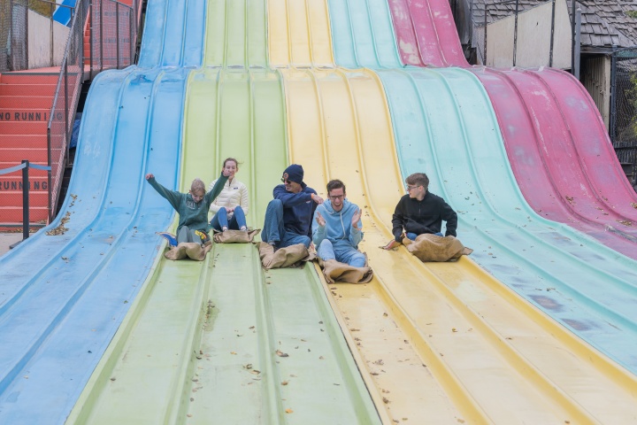 five teenagers sitting on a multi-lane, multi-color slide