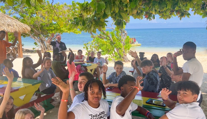 a group of people sitting at tables outdoors with the ocean in the background