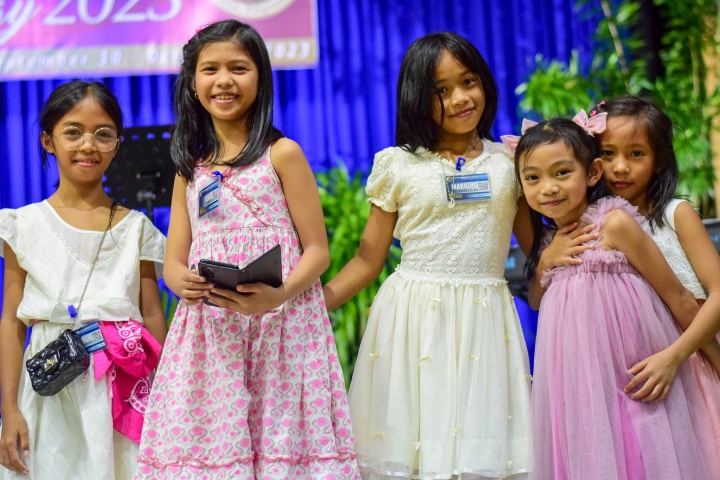 a group of five girls standing indoors and wearing pink and white dresses