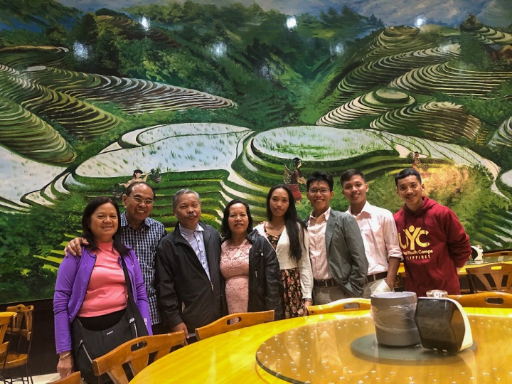 a group of people standing and smiling in front of a painting of a terraced green landscape