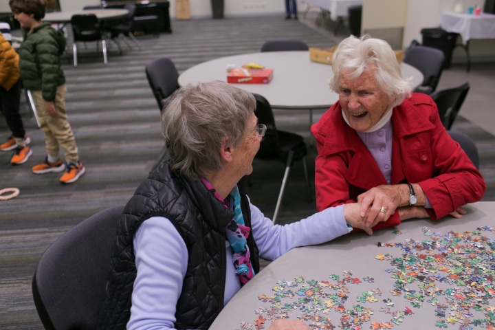 two ladies seated at a table covered with puzzle pieces