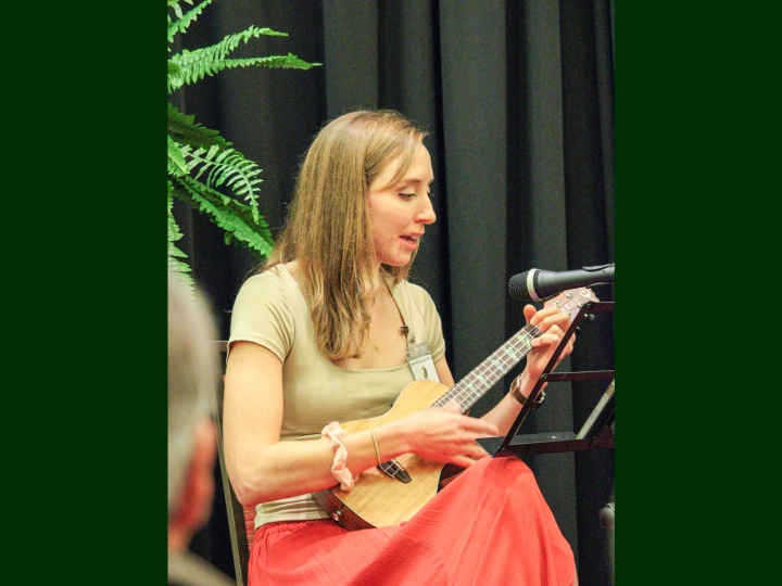 a woman playing a ukulele onstage with a microphone