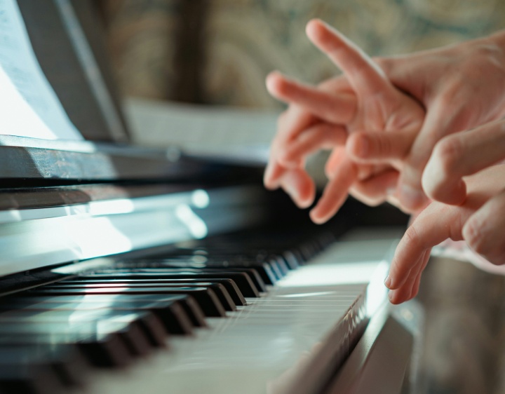 A piano instructor guiding the fingers of child on the piano.