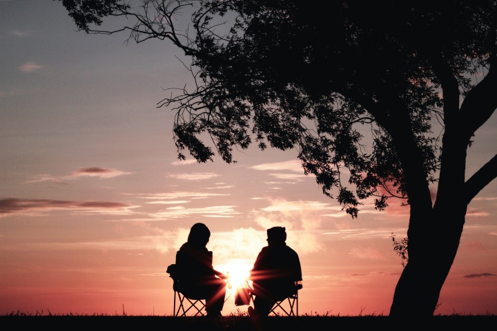 Two people sitting in camp chairs under a tree.