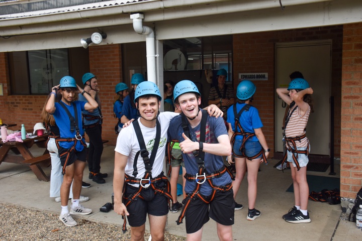 a group of teenagers with helmets and climbing harnesses standing in front of a building