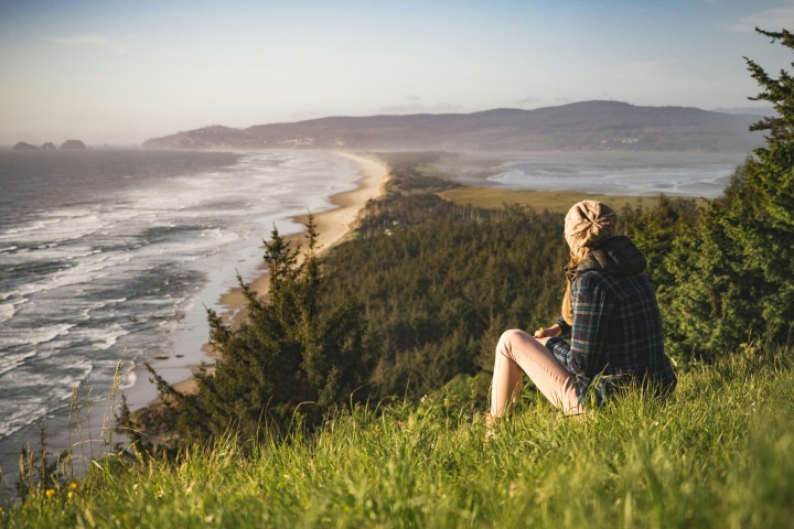 a woman sitting in the grass and looking towards the ocean shore