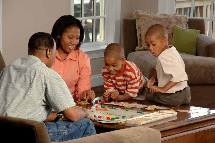 a couple and two boys sitting around a table and playing a board game