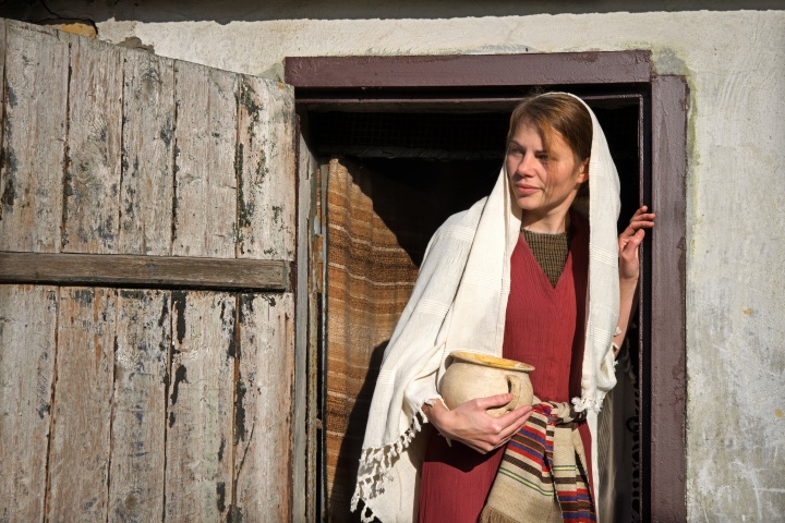 a woman in biblical robes holding a jar and standing in a doorway