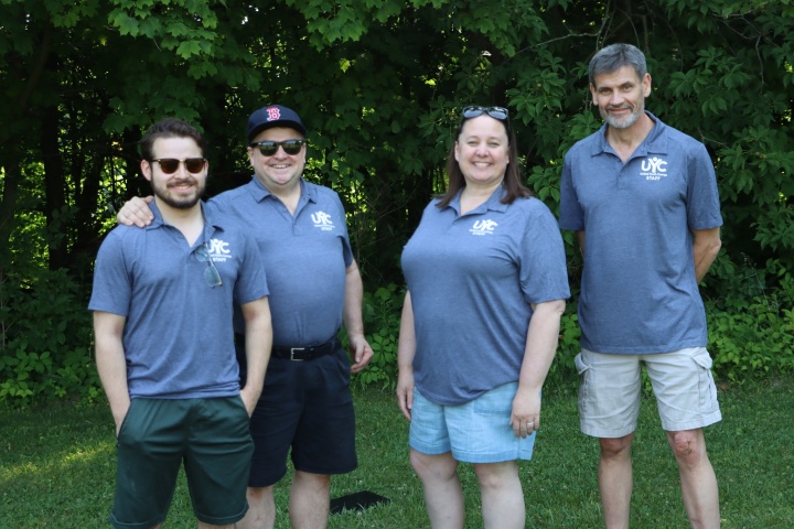 four people standing outdoors with matching camp shirts