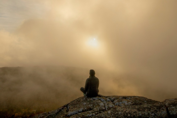 A person sitting on a rock in the morning fog.