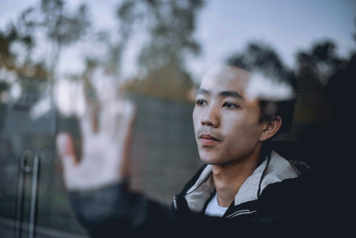 a man's face and outstretched hand behind a glass window