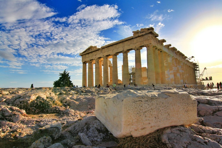 Ancient ruins of the Parthenon with tourists by the structure and a large block of stone in the foreground