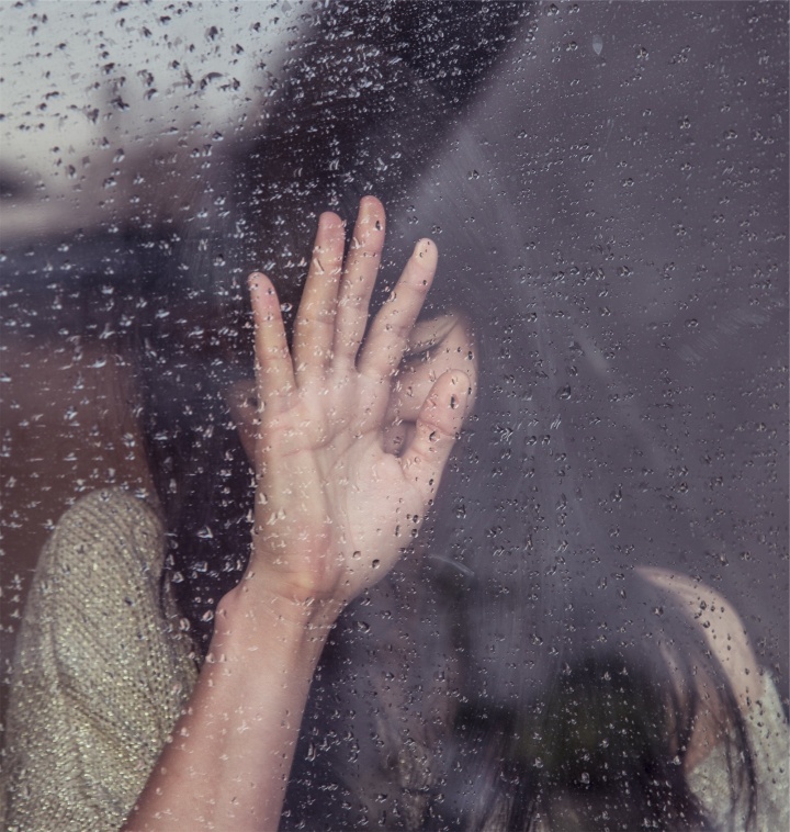 A woman behind a rain covered window.