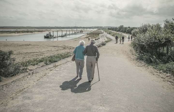 An elder couple walking together on a paved path.