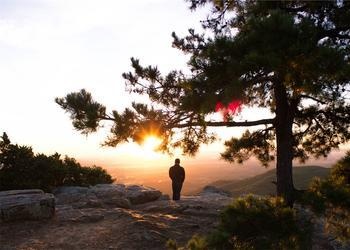 A person looking at the sun setting over a valley.