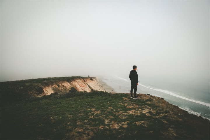 A man looking over a cliff toward the ocean.