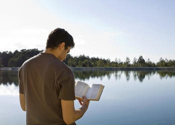 A man reading a Bible outside by a lake.