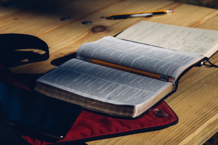 An open Bible on a table with a notebook and pencils and pens.