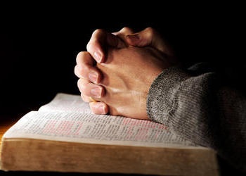 Hands folded on top of a Bible.