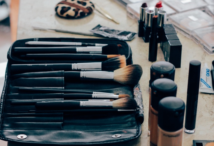 Makeup brushes, powder, lipstick on a table.