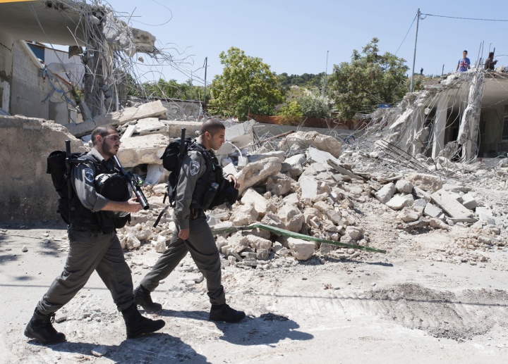 Two soldiers walking in street full of concrete rubble.