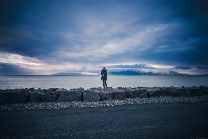 W woman standing on big rocks looking out at cold water.