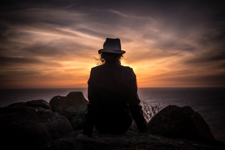 A person sitting on a rock looking over water - orange sunset.