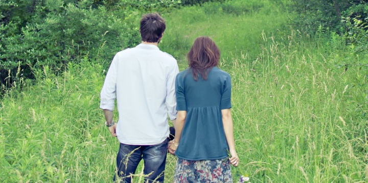 A young married couple holding hands standing in a grass field.