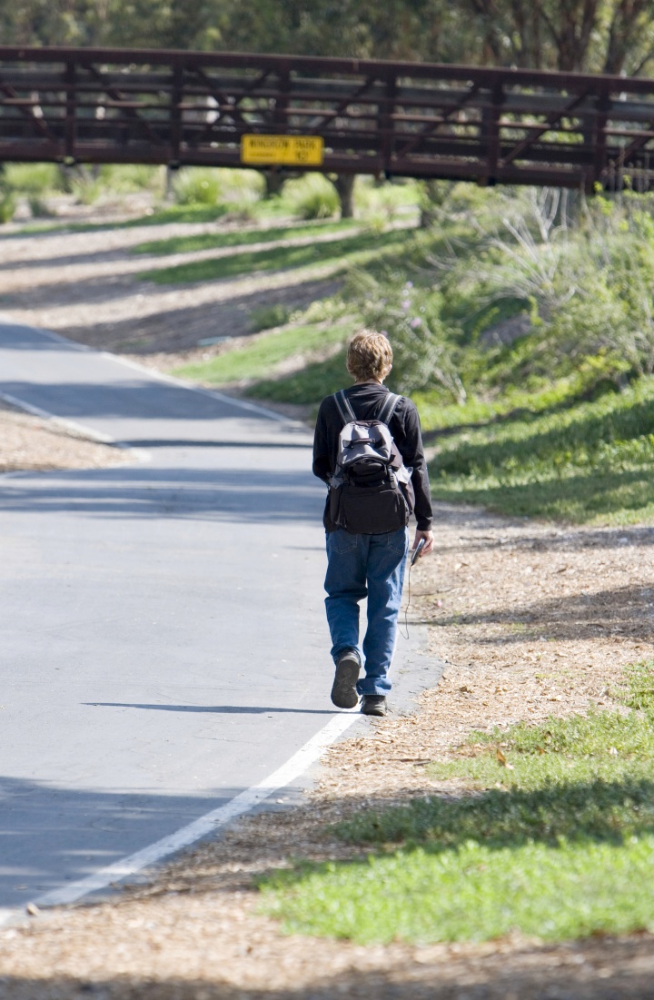 A young boy walking away wearing a backpack.