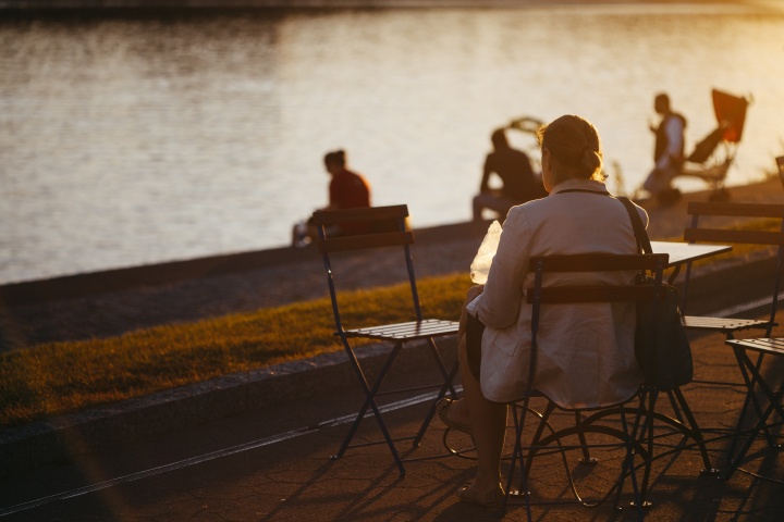 A woman sitting at table outside by a lake watching people.