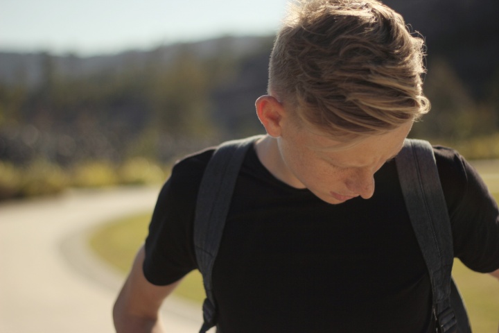 A young man looking down wearing a backpack.