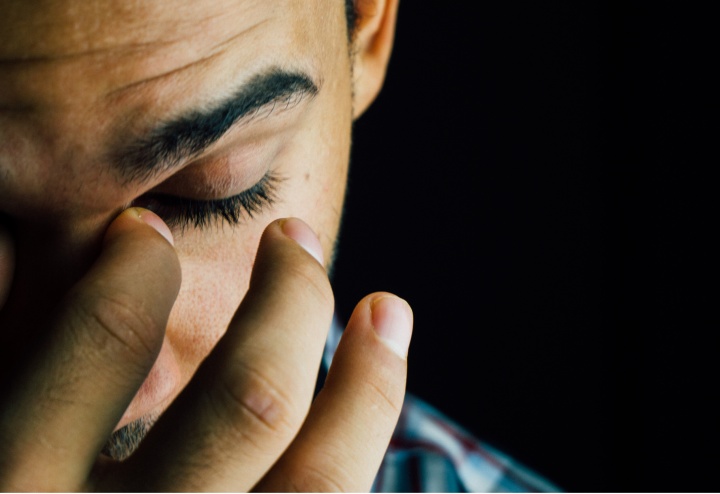 A young man holding his fingers over his eyes.