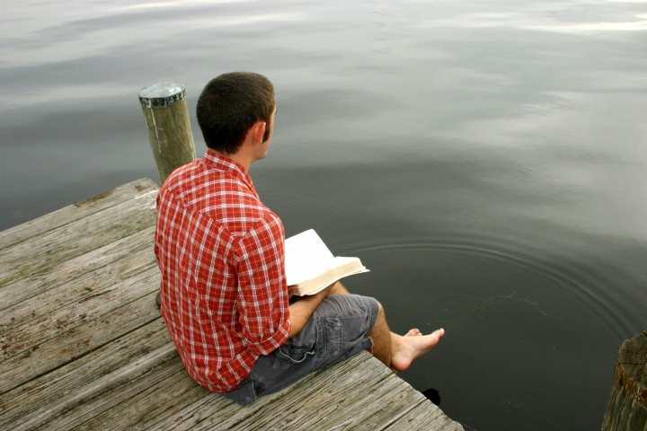 A man sitting on a dock reading a Bible.