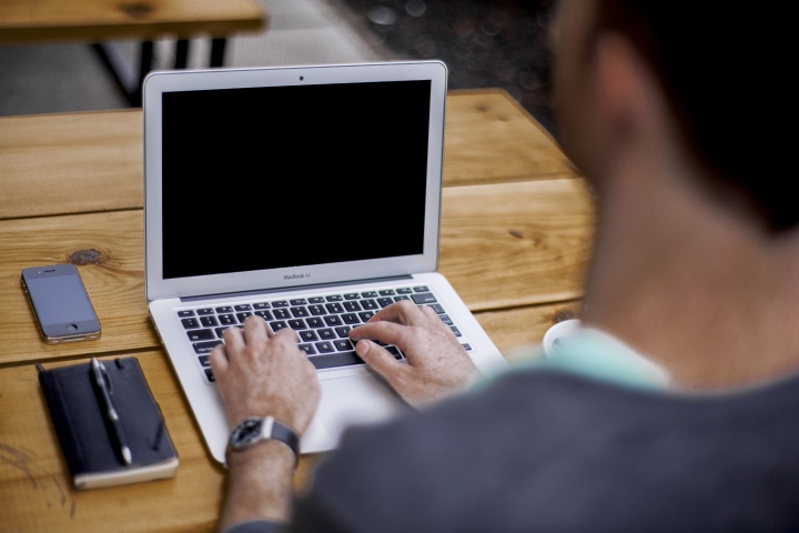 A man typing on a laptop while sitting a desk.