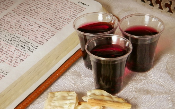 A Bible open to the book of John, small cups of wine and some broken unleavened bread.