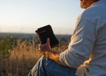 A man sitting on the ground holding an old Bible.