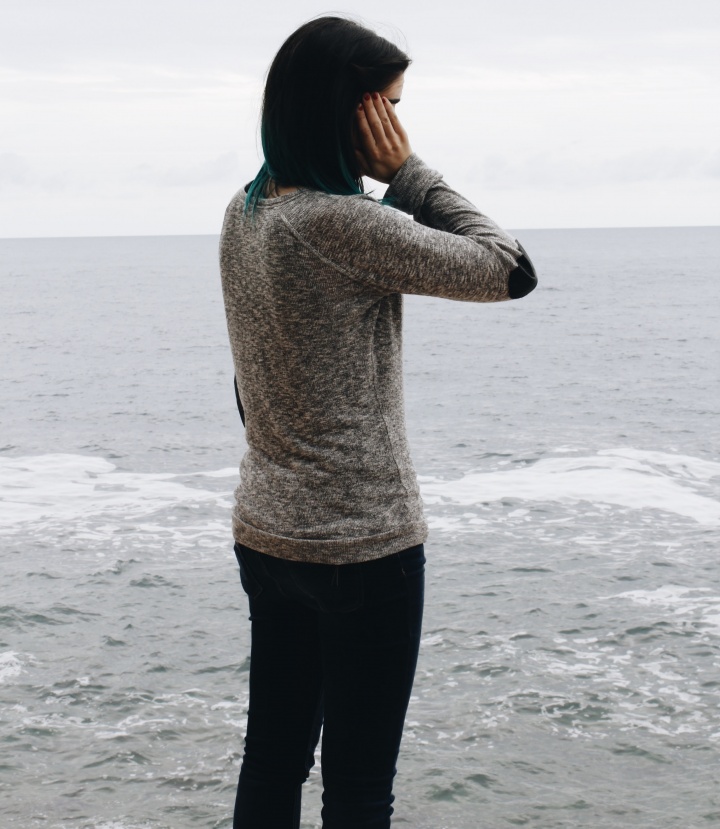 A woman standing by the ocean with hand on head.