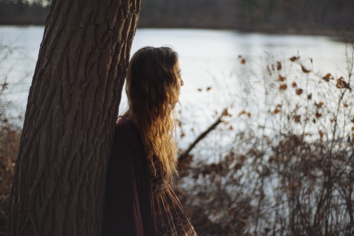 A young woman leaning up against a tree.