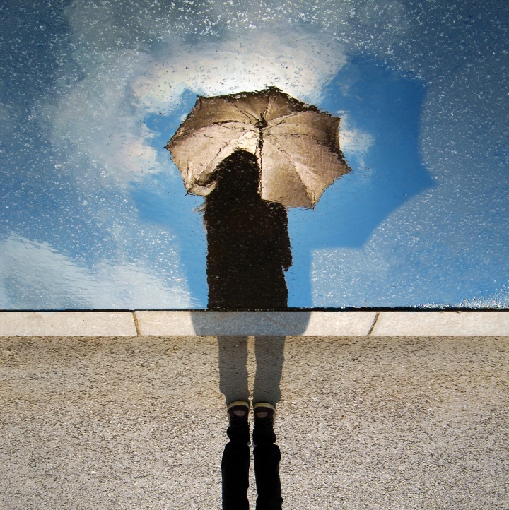 A person holding an umbrella and looking at their shadow.