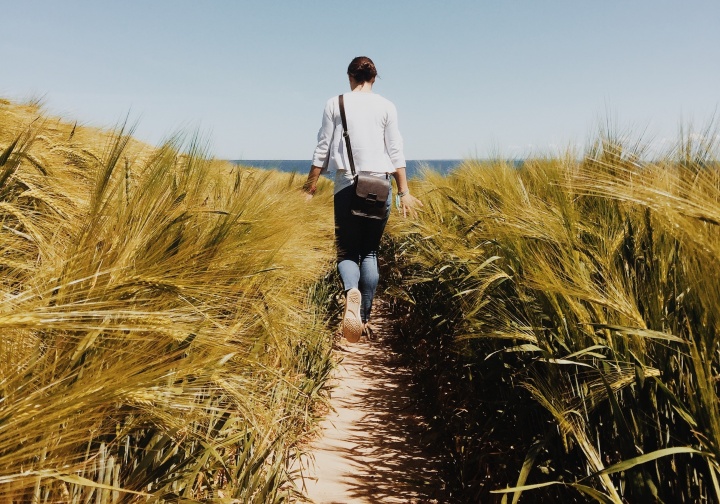 A woman walking on a path with tall grass around her.