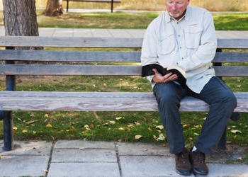 A man sitting on a bench reaching the Bible.