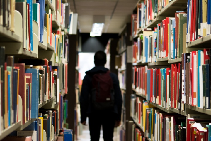 A person walking in a library surrounded by stacks of books.