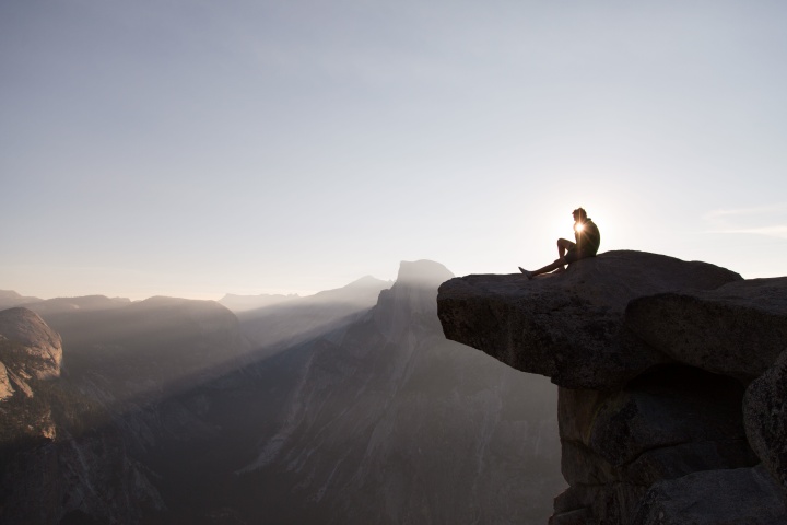 A man sitting on the edge of mountain cliff thinking.