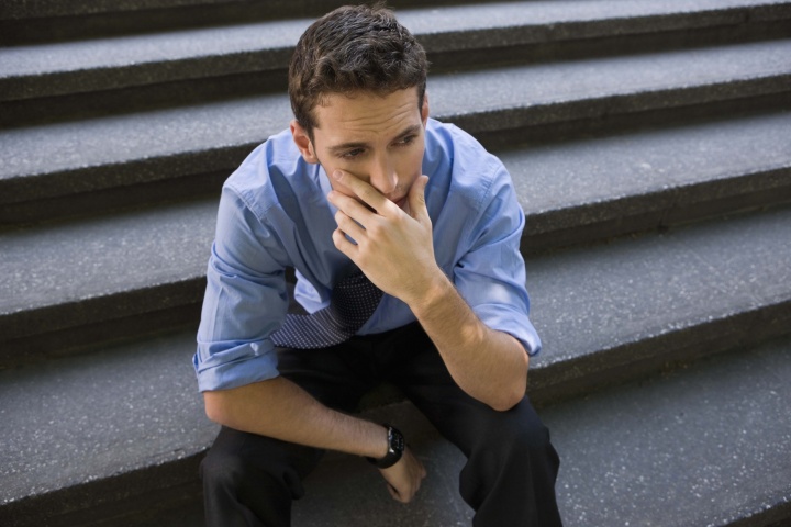 A young man sitting on concrete steps with his chin resting on his hands.
