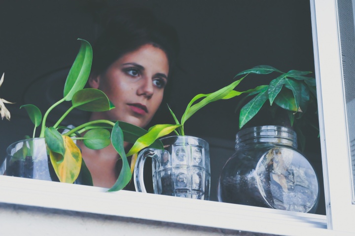 A woman looking outside a window with plants on the ledge.