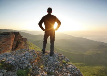 A young man standing at the edge of cliff looking at the setting sun.