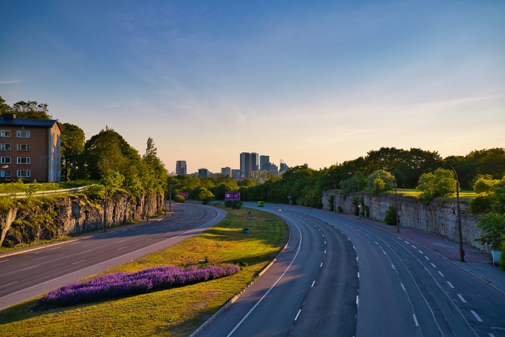 a two-sided highway running through a green landscape with historical buildings, and a cityscape in the background