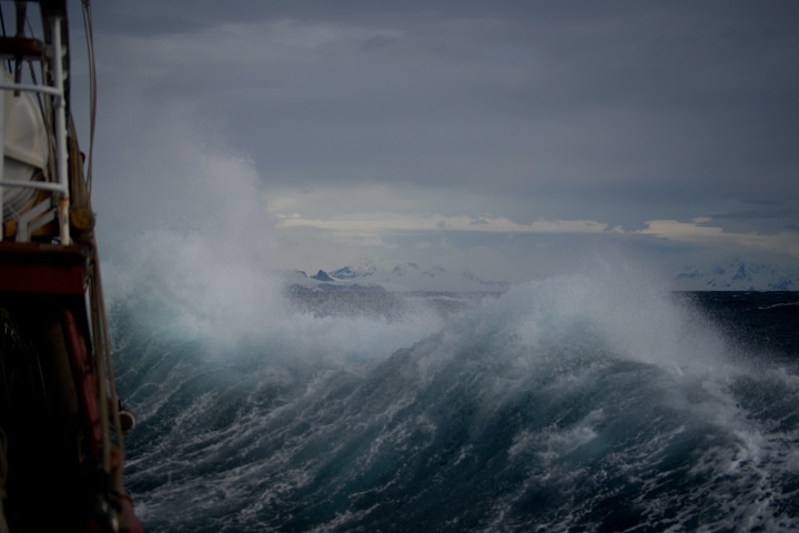 Photo of a stormy sea taken from a ship. The waves are crashing against the ship and the sky is filled with low gray clouds.