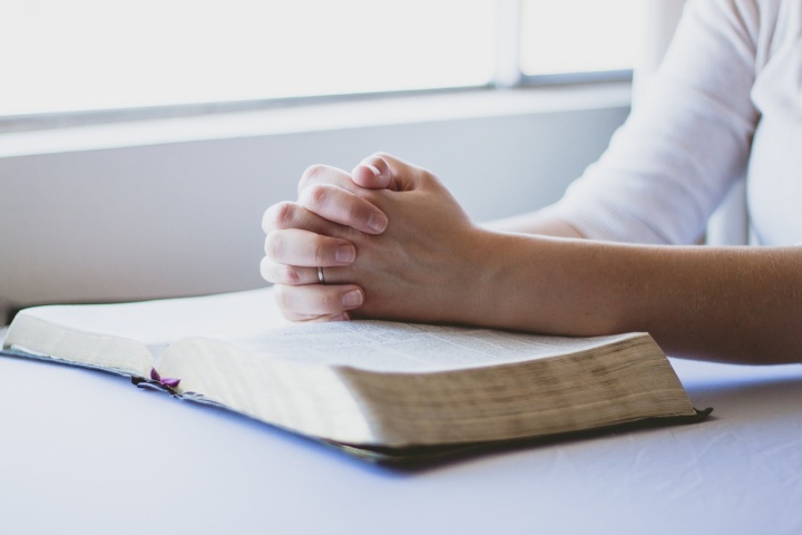 a pair of folded hands on an open Bible